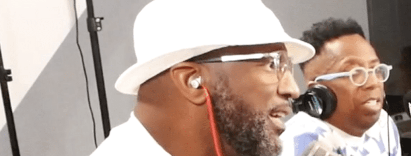 Two men speaking into microphones, wearing hats.